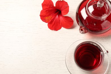 Photo of Delicious hibiscus tea in glass cup, teapot and flower on light wooden table, flat lay. Space for text
