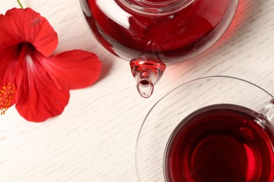 Photo of Delicious hibiscus tea in glass cup, teapot and flower on light wooden table, flat lay