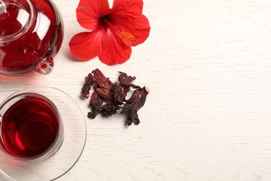 Photo of Delicious hibiscus tea in glass cup, teapot, dry roselle sepals and flower on light wooden table, flat lay. Space for text