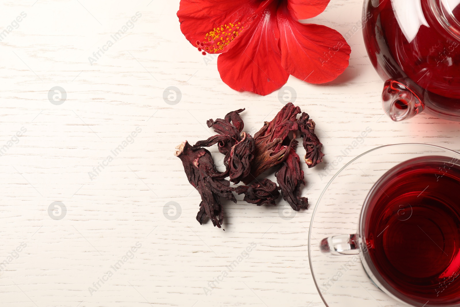 Delicious hibiscus tea in glass cup, teapot, dry roselle sepals and flower on light wooden table, flat lay. Space for text Photo of Delicious hibiscus tea in glass cup, teapot, dry roselle sepals and flower on light wooden table, flat lay. Space for text