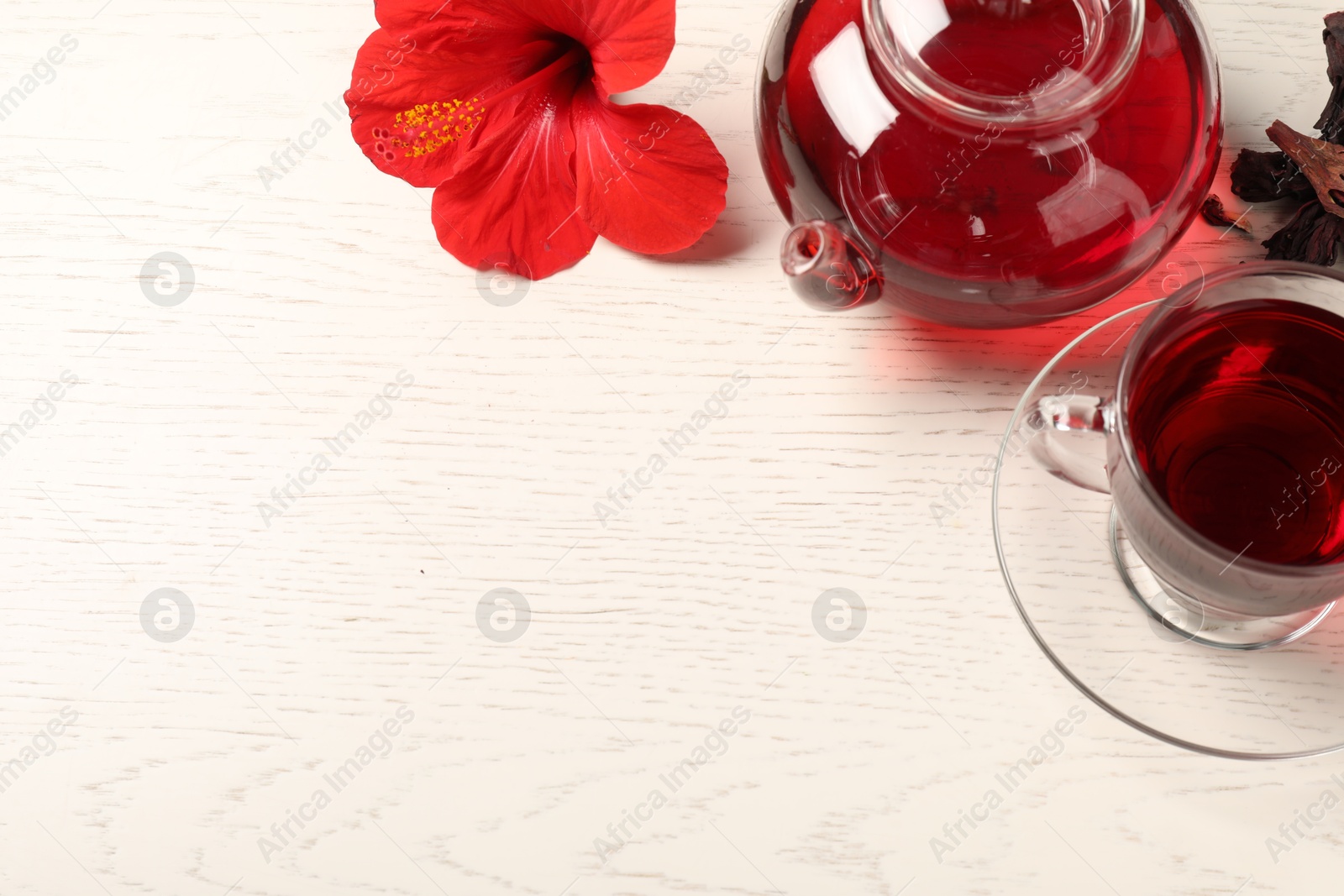Delicious hibiscus tea in glass cup, teapot, dry roselle sepals and flower on light wooden table, above view Photo of Delicious hibiscus tea in glass cup, teapot, dry roselle sepals and flower on light wooden table, above view