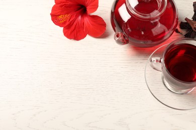 Photo of Delicious hibiscus tea in glass cup, teapot, dry roselle sepals and flower on light wooden table, above view