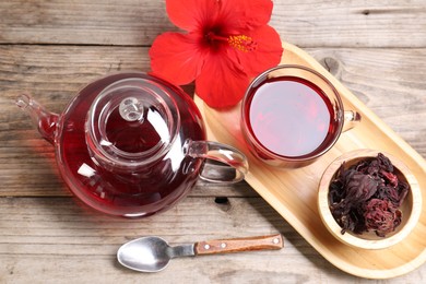 Photo of Delicious hibiscus tea in glass cup, teapot, dry roselle sepals and flower on wooden table, above view