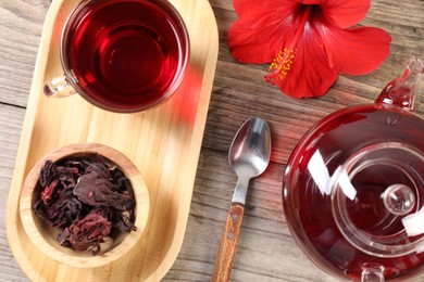 Photo of Delicious hibiscus tea in glass cup, teapot, dry roselle sepals and flower on wooden table, flat lay