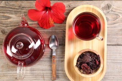 Photo of Delicious hibiscus tea in glass cup, teapot, dry roselle sepals and flower on wooden table, flat lay
