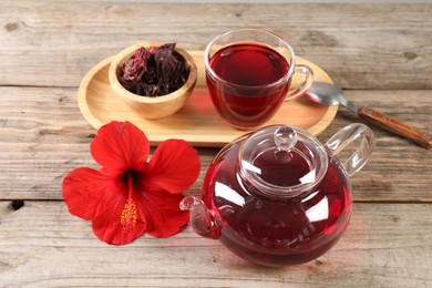 Photo of Delicious hibiscus tea in glass cup, teapot, dry roselle sepals and flower on wooden table