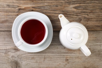 Photo of Delicious hibiscus tea in cup and teapot on wooden table, flat lay