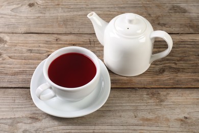 Photo of Delicious hibiscus tea in cup and teapot on wooden table