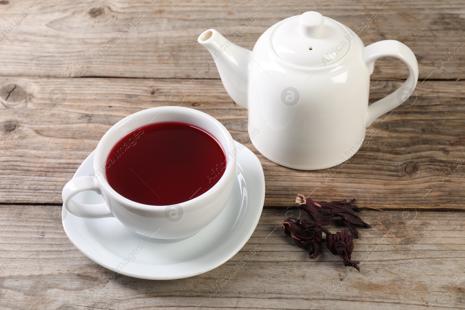 Delicious hibiscus tea in cup, teapot and dry roselle sepals on wooden table Photo of Delicious hibiscus tea in cup, teapot and dry roselle sepals on wooden table