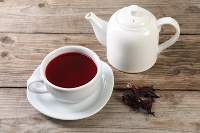 Photo of Delicious hibiscus tea in cup, teapot and dry roselle sepals on wooden table