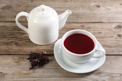 Photo of Delicious hibiscus tea in cup, teapot and dry roselle sepals on wooden table