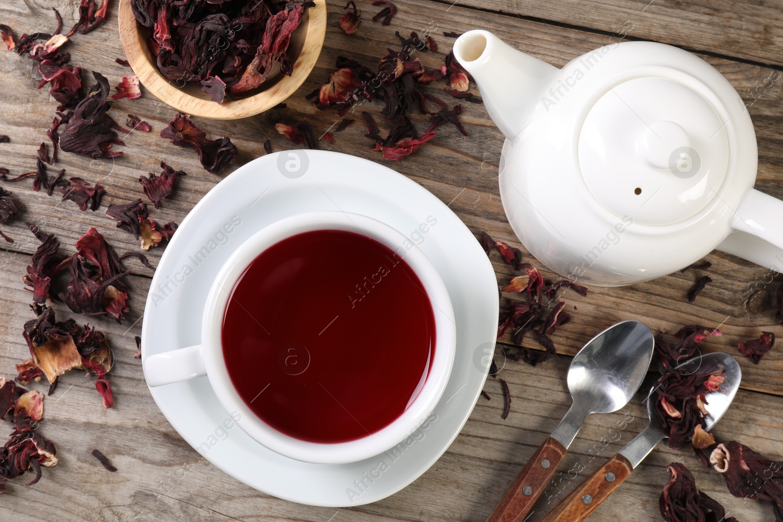 Delicious hibiscus tea in cup, teapot, dry roselle sepals and spoons on wooden table, flat lay Photo of Delicious hibiscus tea in cup, teapot, dry roselle sepals and spoons on wooden table, flat lay