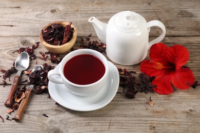 Photo of Delicious hibiscus tea in cup, teapot, dry roselle sepals and flower on wooden table