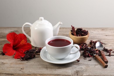 Photo of Delicious hibiscus tea in cup, teapot, dry roselle sepals and flower on wooden table