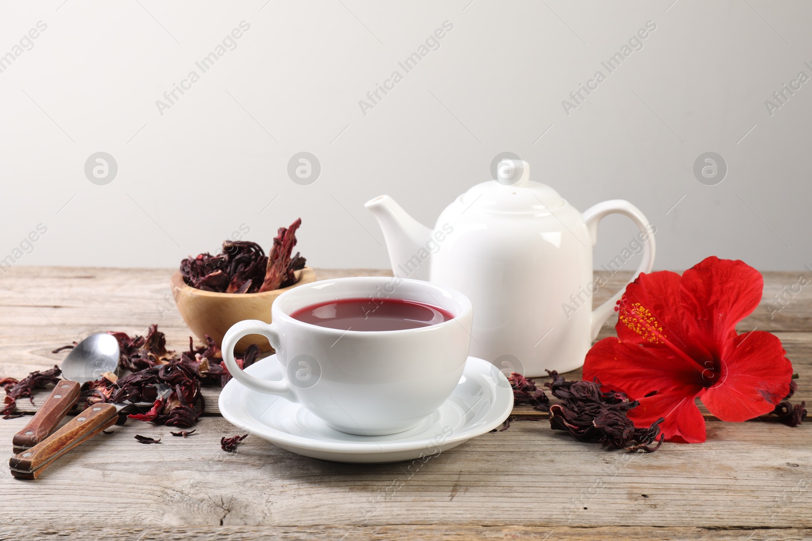 Delicious hibiscus tea in cup, teapot, dry roselle sepals and flower on wooden table Photo of Delicious hibiscus tea in cup, teapot, dry roselle sepals and flower on wooden table