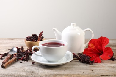 Photo of Delicious hibiscus tea in cup, teapot, dry roselle sepals and flower on wooden table