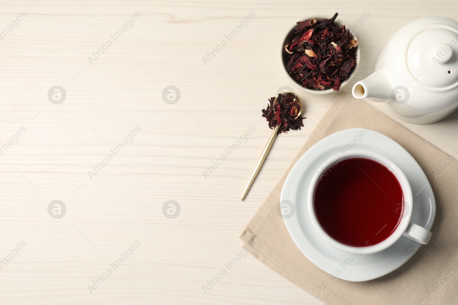 Delicious hibiscus tea in cup, teapot, dry roselle sepals and spoon on light wooden table, flat lay. Space for text Photo of Delicious hibiscus tea in cup, teapot, dry roselle sepals and spoon on light wooden table, flat lay. Space for text