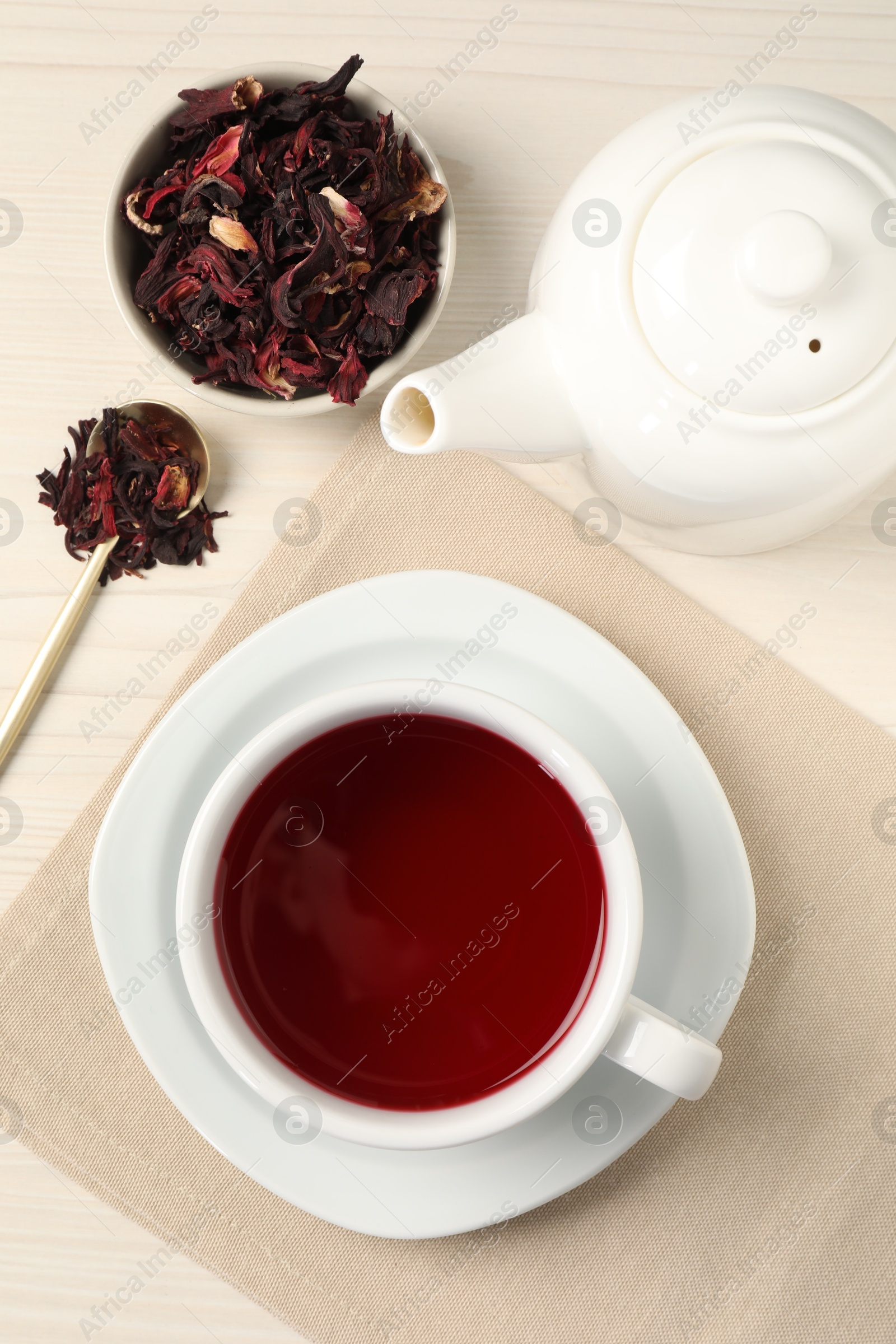 Delicious hibiscus tea in cup, teapot, dry roselle sepals and spoon on light wooden table, flat lay Photo of Delicious hibiscus tea in cup, teapot, dry roselle sepals and spoon on light wooden table, flat lay