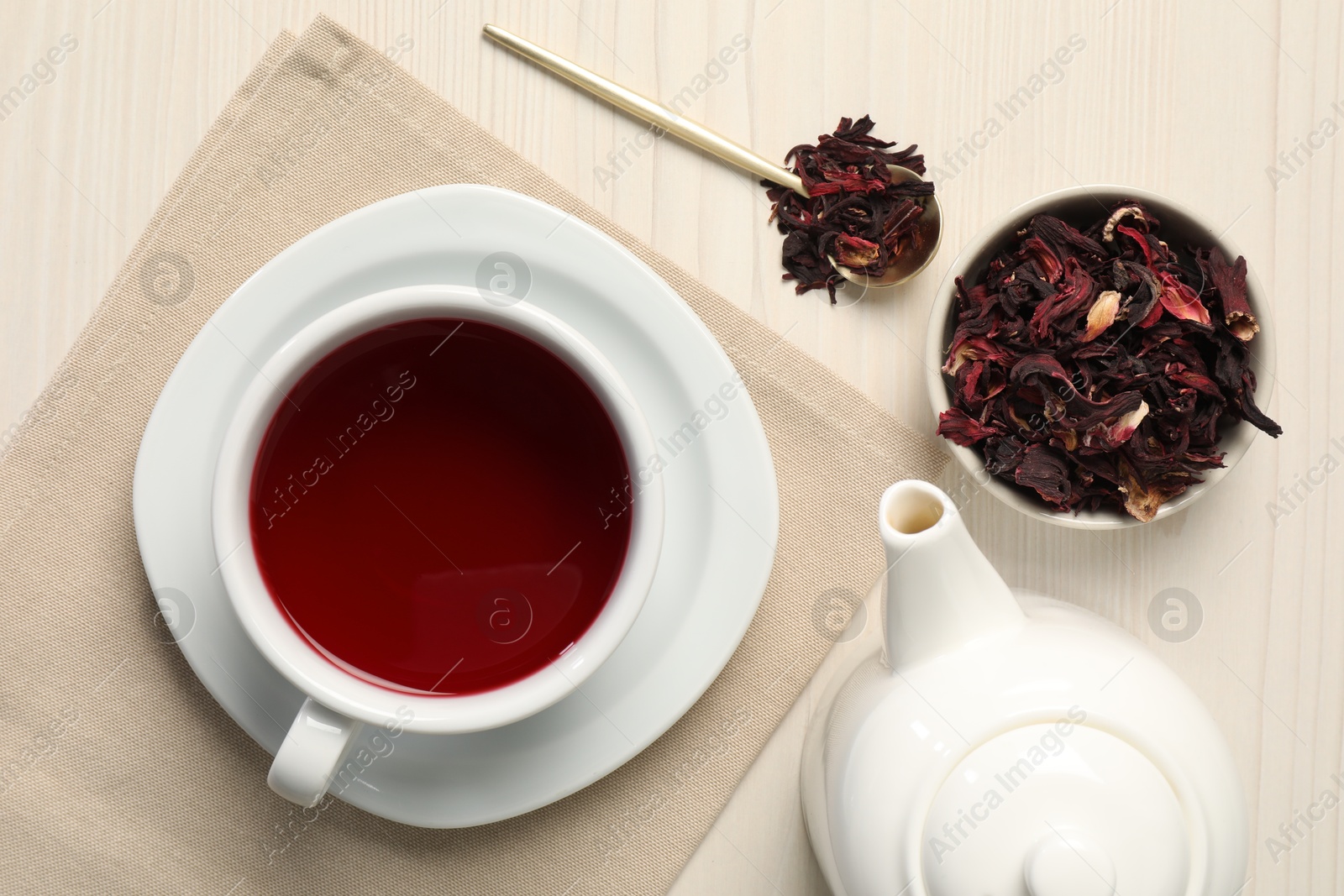Delicious hibiscus tea in cup, teapot, dry roselle sepals and spoon on light wooden table, flat lay Photo of Delicious hibiscus tea in cup, teapot, dry roselle sepals and spoon on light wooden table, flat lay