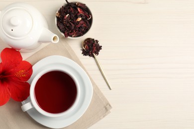 Photo of Delicious hibiscus tea in cup, teapot, dry roselle sepals and flower on light wooden table, flat lay. Space for text