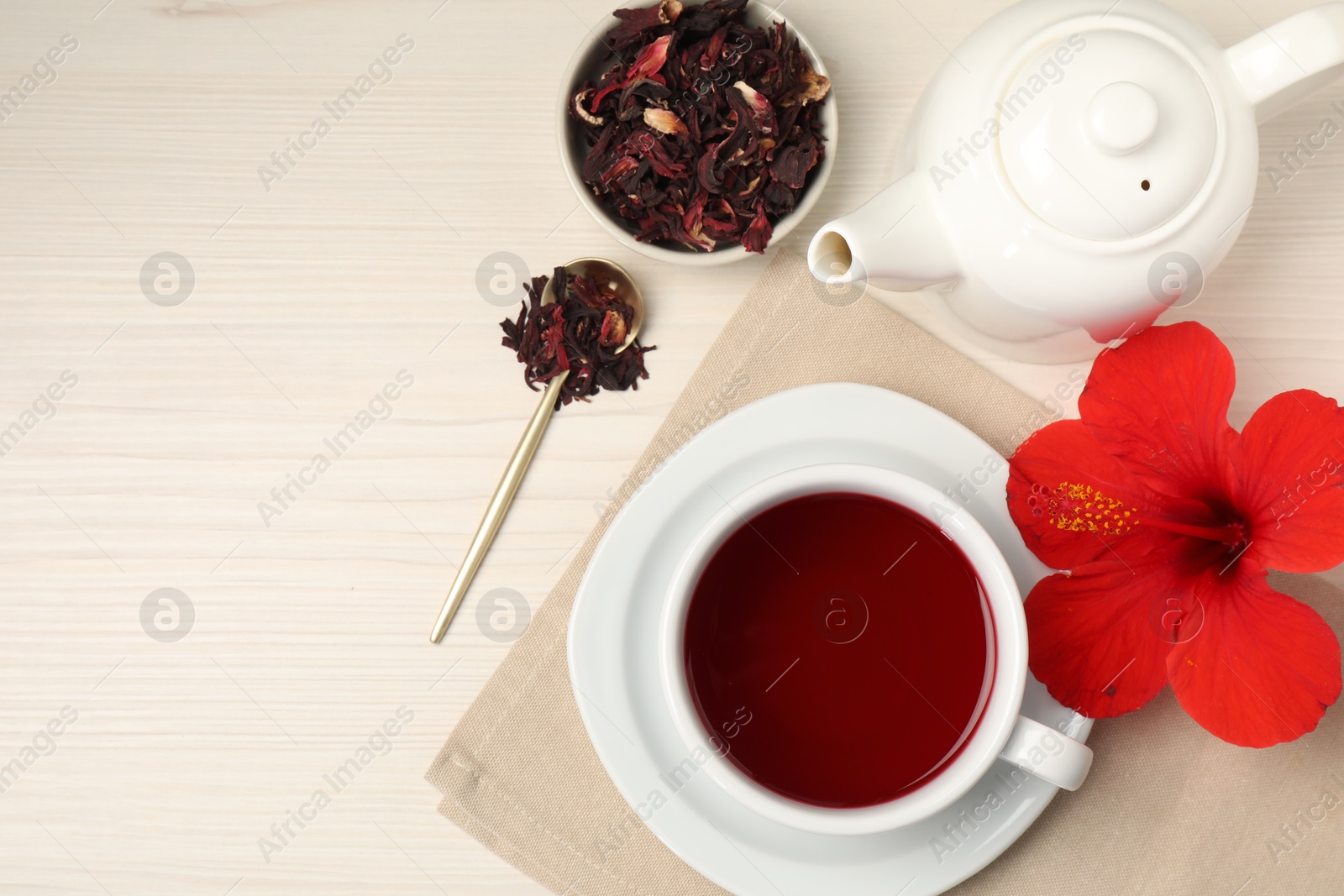 Delicious hibiscus tea in cup, teapot, dry roselle sepals and flower on light wooden table, flat lay. Space for text Photo of Delicious hibiscus tea in cup, teapot, dry roselle sepals and flower on light wooden table, flat lay. Space for text