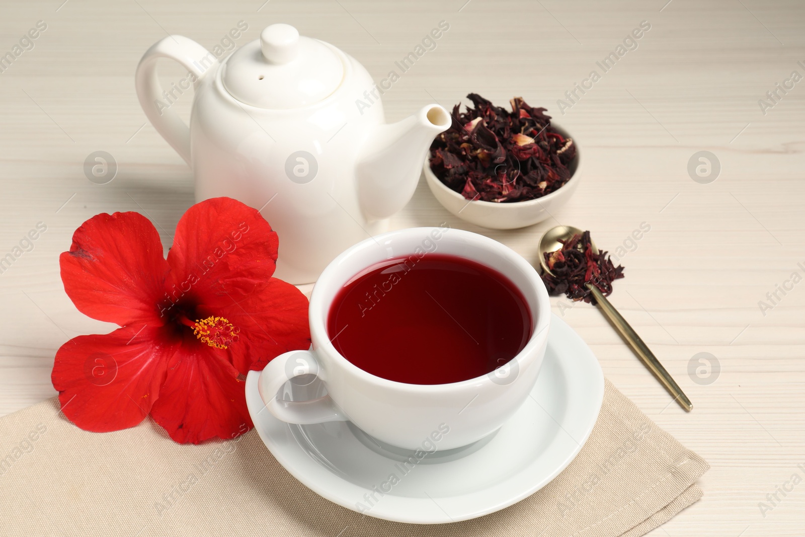 Delicious hibiscus tea in cup, teapot, dry roselle sepals and flower on light wooden table Photo of Delicious hibiscus tea in cup, teapot, dry roselle sepals and flower on light wooden table