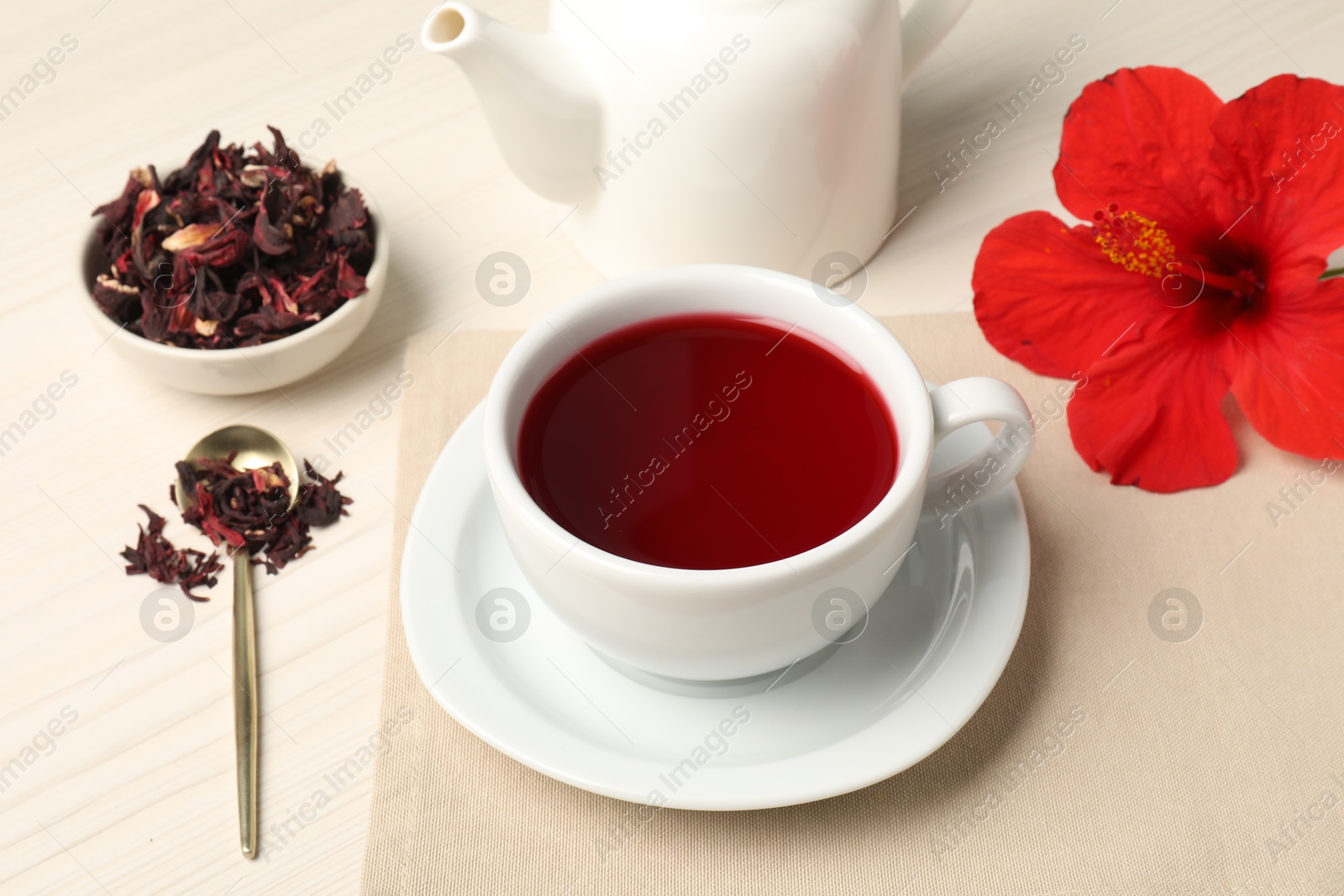 Delicious hibiscus tea in cup, teapot, dry roselle sepals and flower on light wooden table, closeup Photo of Delicious hibiscus tea in cup, teapot, dry roselle sepals and flower on light wooden table, closeup
