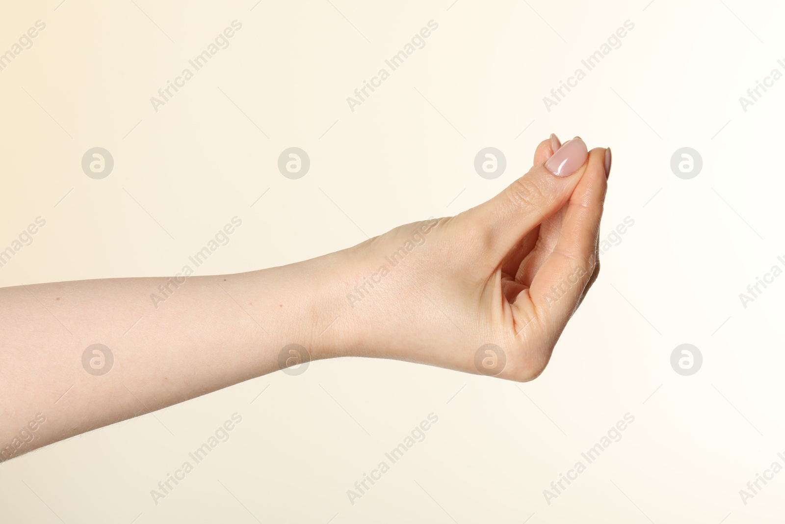 Woman holding something in hand on beige background, closeup Photo of Woman holding something in hand on beige background, closeup
