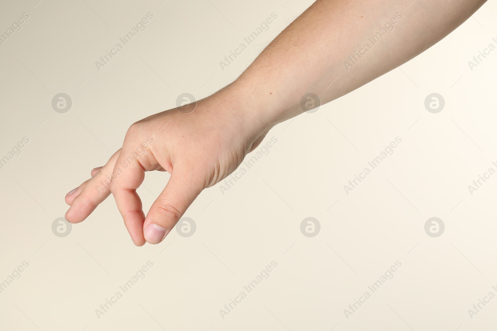 Man holding something in hand on beige background, closeup Photo of Man holding something in hand on beige background, closeup