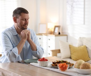 Photo of Man praying before dinner at table indoors. Space for text