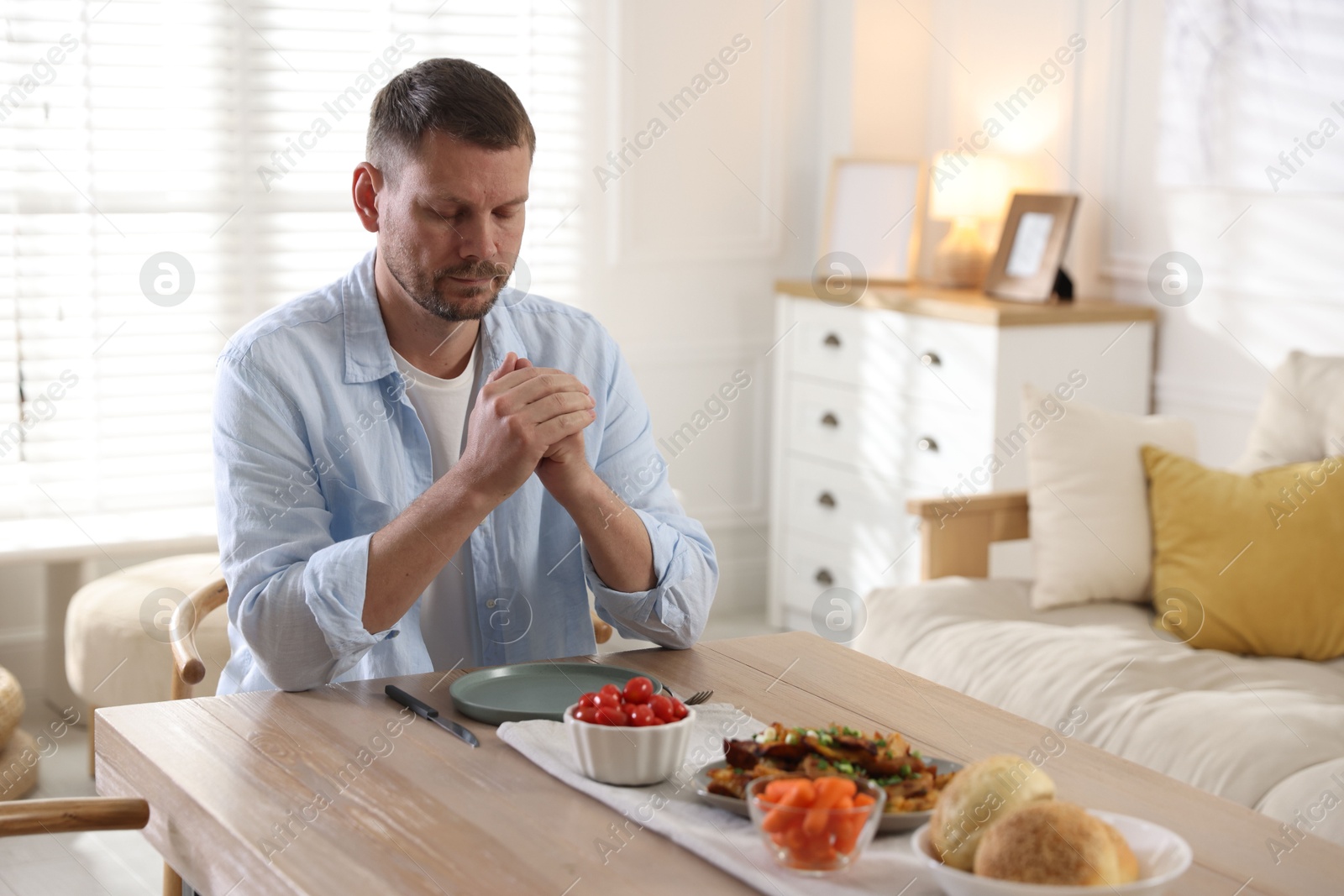 Man praying before dinner at table indoors. Space for text Photo of Man praying before dinner at table indoors. Space for text