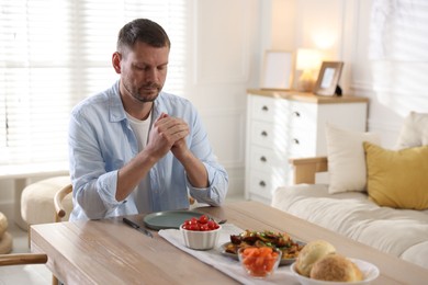 Photo of Man praying before dinner at table indoors. Space for text