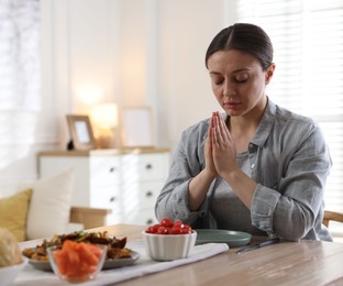 Photo of Woman praying before dinner at table indoors. Space for text