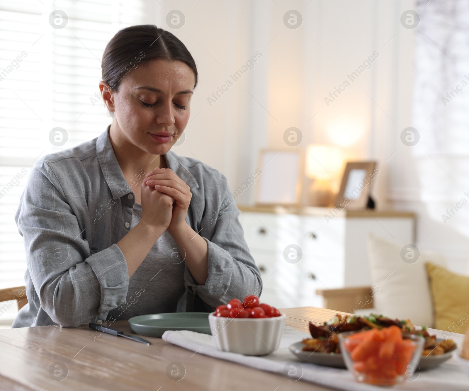 Woman praying before dinner at table indoors. Space for text Photo of Woman praying before dinner at table indoors. Space for text