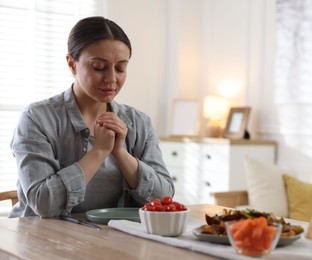 Photo of Woman praying before dinner at table indoors. Space for text