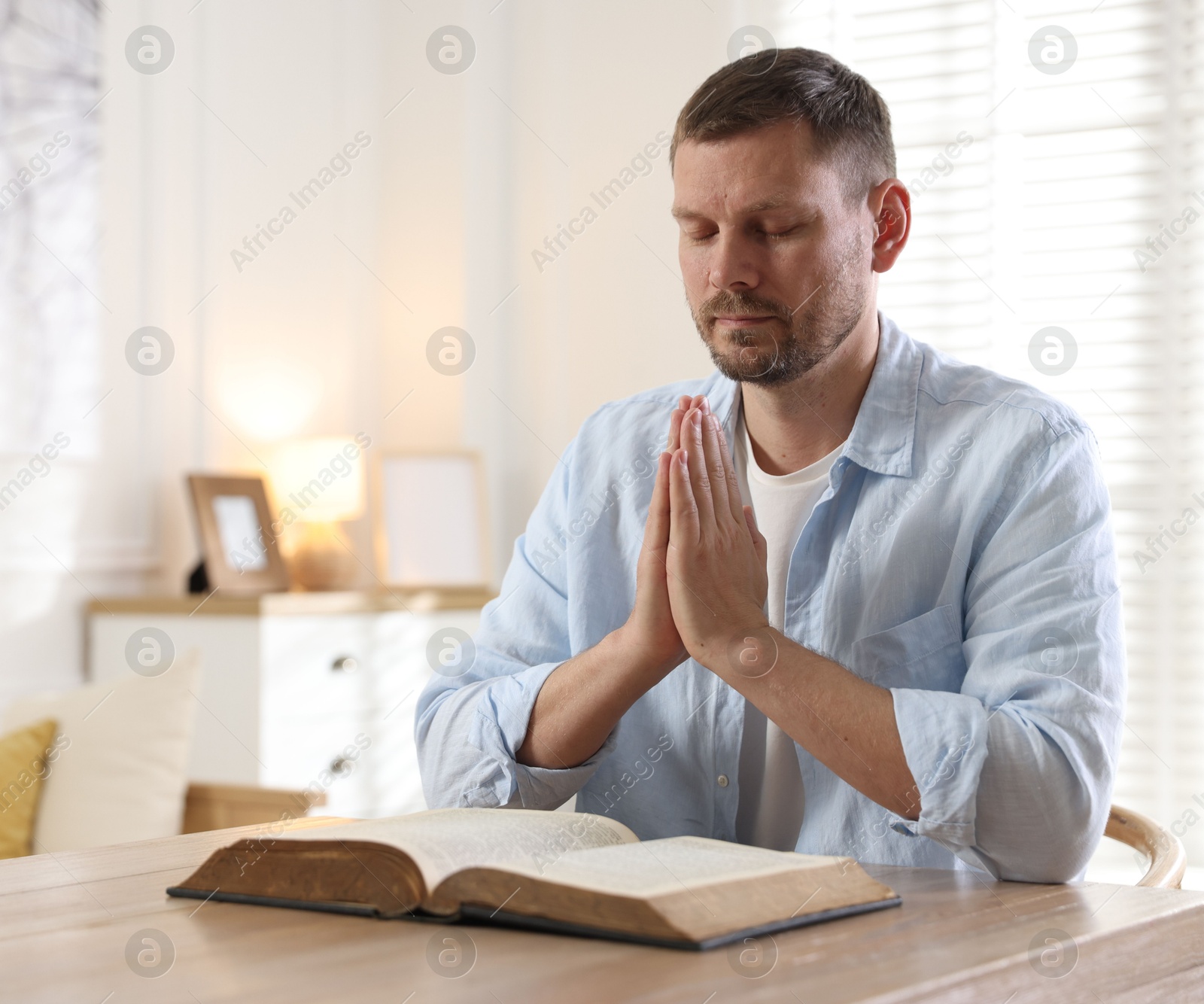 Man with Bible praying at table indoors. Space for text Photo of Man with Bible praying at table indoors. Space for text