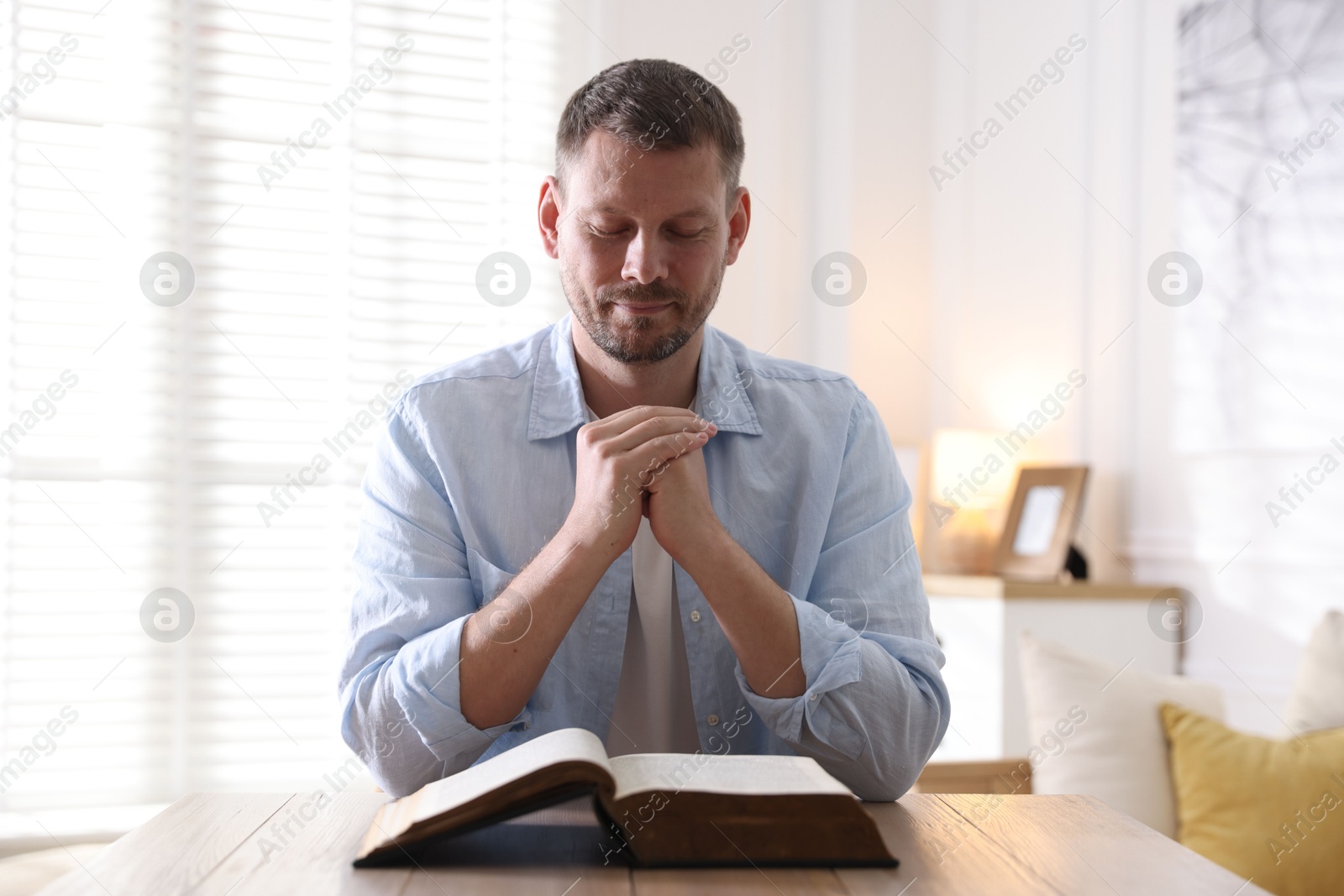 Photo of Man with Bible praying at table indoors