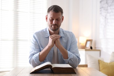 Photo of Man with Bible praying at table indoors