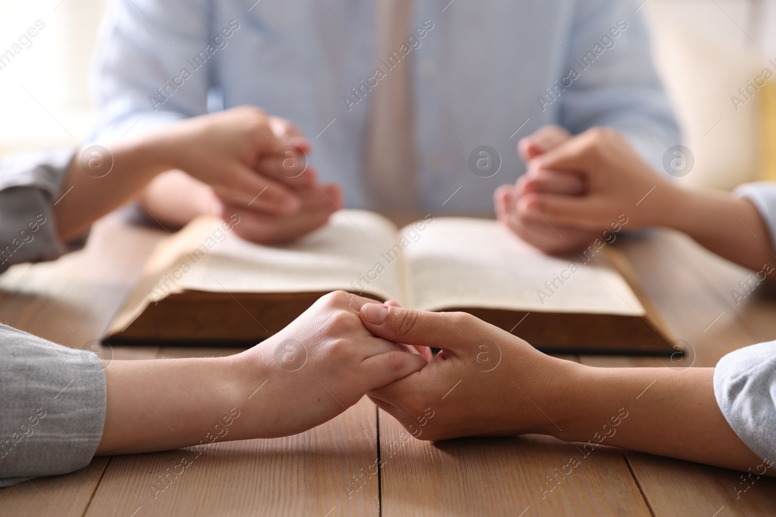 Family with Bible praying at wooden table indoors, closeup Photo of Family with Bible praying at wooden table indoors, closeup