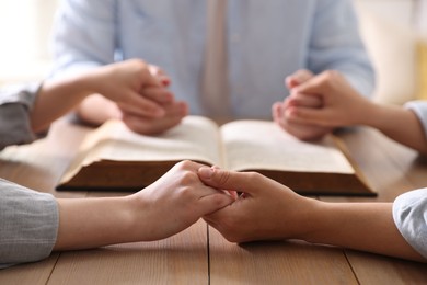 Photo of Family with Bible praying at wooden table indoors, closeup