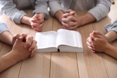 Photo of Family with Bible praying at wooden table indoors, closeup