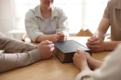 Photo of Family with Bible praying at wooden table indoors, closeup