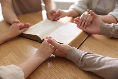 Photo of Family with Bible praying at wooden table indoors, closeup