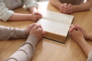Photo of Family with Bible praying at wooden table indoors, closeup