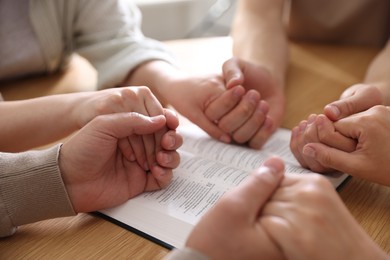 Photo of Family with Bible praying at wooden table indoors, closeup