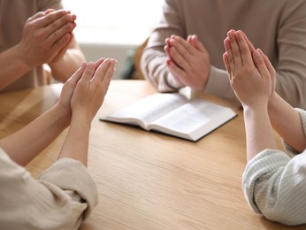 Photo of Family with Bible praying at wooden table indoors, closeup