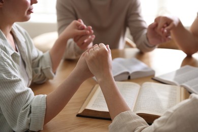 Photo of Family with Bibles praying at wooden table indoors, closeup