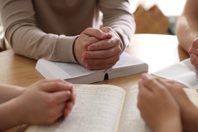 Photo of Family with Bibles praying at wooden table indoors, closeup