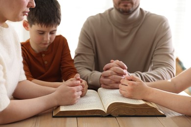 Photo of Family with Bible praying at table indoors, closeup