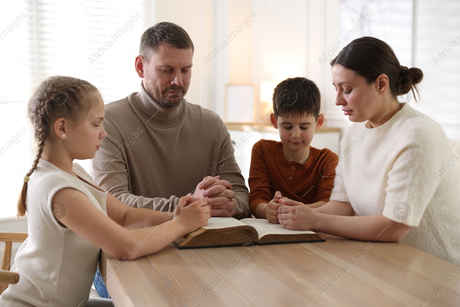 Family with Bible praying at table indoors Photo of Family with Bible praying at table indoors